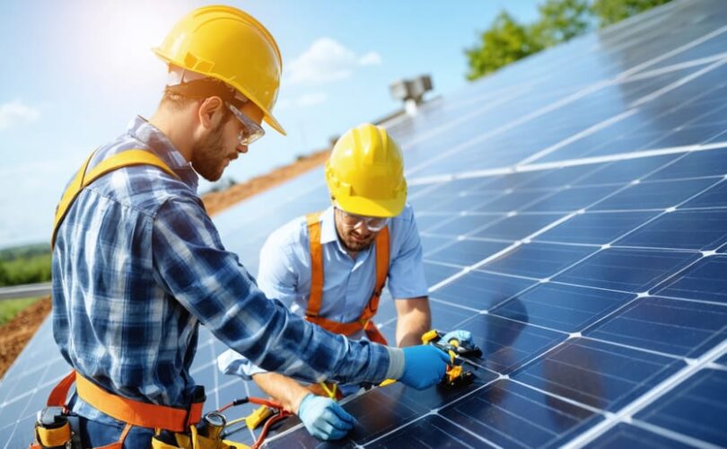 Workers wearing comprehensive personal protective equipment conducting a safe solar panel installation with focus on fall protection and electrical safety at a sunny site.