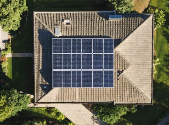 "Aerial view of a house with a fully equipped 5kW solar panel array on the roof, surrounded by lush greenery and neighboring homes."