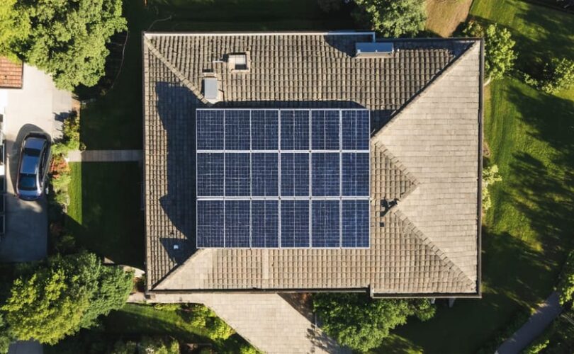 "Aerial view of a house with a fully equipped 5kW solar panel array on the roof, surrounded by lush greenery and neighboring homes."