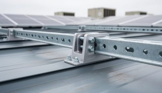 Aluminum Roofclamp™ bracket clamping onto a standing-seam metal roof with Unistrut-style framing supporting a solar PV array, shown in sharp detail on a commercial rooftop.