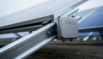 Close-up of a solar PV mounting rail and junction box with corrosion-resistant metal surfaces outdoors under soft daylight.