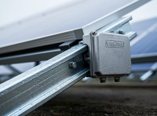 Close-up of a solar PV mounting rail and junction box with corrosion-resistant metal surfaces outdoors under soft daylight.