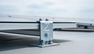 Close-up of a Z-shaped solar mounting bracket securing a horizontally oriented photovoltaic panel on a flat commercial rooftop.