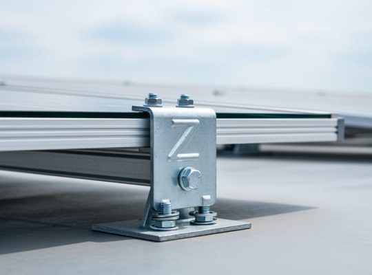 Close-up of a Z-shaped solar mounting bracket securing a horizontally oriented photovoltaic panel on a flat commercial rooftop.