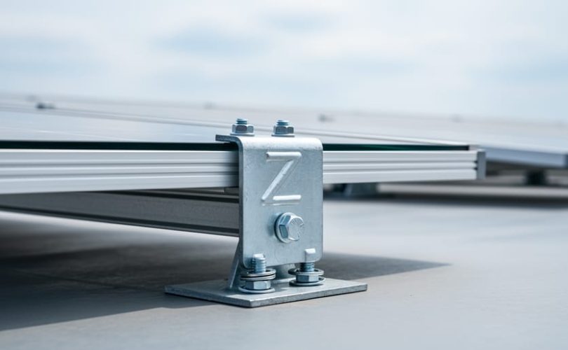 Close-up of a Z-shaped solar mounting bracket securing a horizontally oriented photovoltaic panel on a flat commercial rooftop.